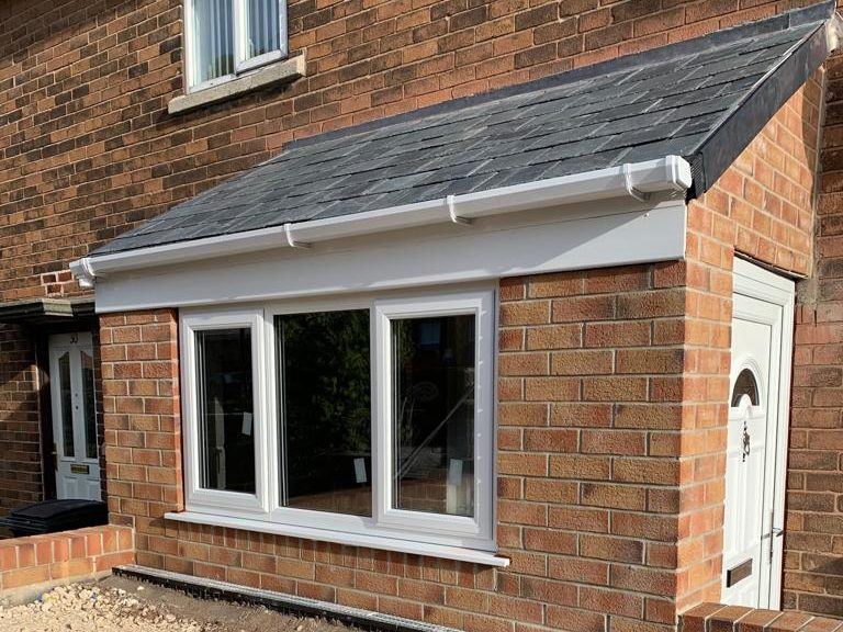 Single-storey brick extension with a slate lean-to roof and white uPVC windows